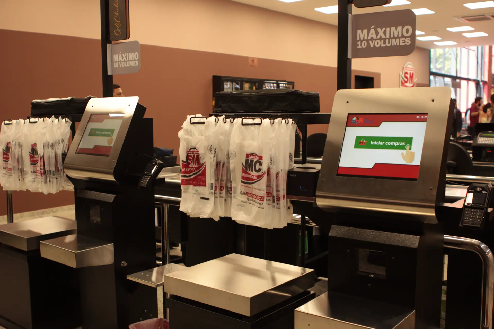 Foto de self checkout em loja, com monitor touch e leitor de pagamentos, ao lado de caixas e sacolas de compras, oferecendo uma estrutura moderna e completa para os consumidores que buscam autonomia e agilidade na finalização de suas compras.